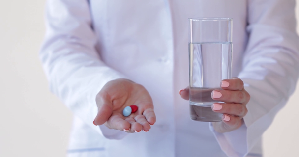 inyección recortada del médico sosteniendo píldoras y vaso de agua en blanco
 - Metraje, vídeo