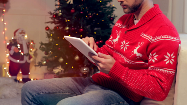 tiro recortado de hombre sentado en el sofá y el uso de la tableta en la sala de estar decorada de Navidad
 - Imágenes, Vídeo