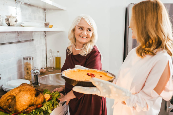smiling senior mother and daughter baking pumpkin pie together at home - Photo, Image