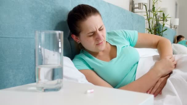 4 k felvétel, fiatal beteg asszony feküdt az ágyban, és szenved a fájdalom a gyomorban iszik tabletta éjjeliszekrény - Felvétel, videó
