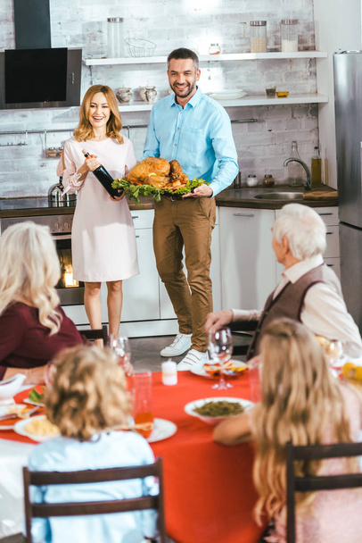 Молодой человек и женщина несут вино и индейку на ужин в честь Дня благодарения с семьей дома
 - Фото, изображение