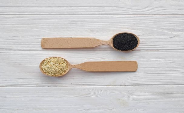Black and white sesame in wooden spoons on a white wooden background. Top view - Photo, Image