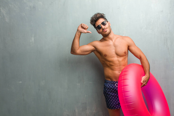 Молодий атлетичний чоловік у купальнику на грандж-стіні гордий і впевнений, вказуючи пальці, наприклад, слідувати концепції задоволення, зарозумілості і здоров'я
 - Фото, зображення