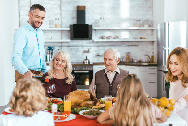 happy family having delicious thanksgiving dinner together at home while father pouring wine - Photo, Image