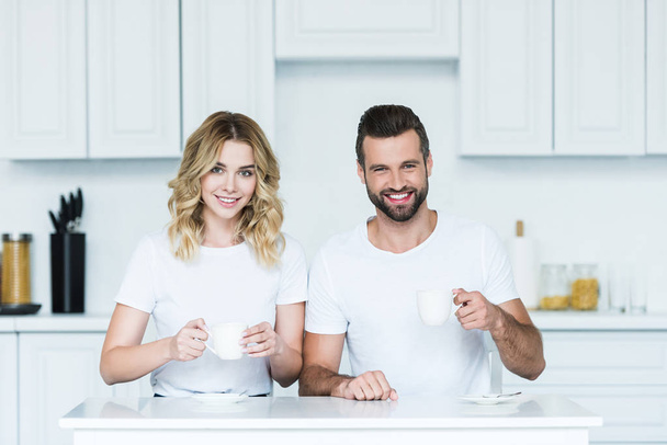 heureux jeune couple tenant des tasses de café et souriant à la caméra
 - Photo, image