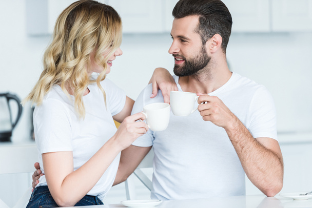 feliz jovem casal segurando xícaras de café e sorrindo uns aos outros
 - Foto, Imagem
