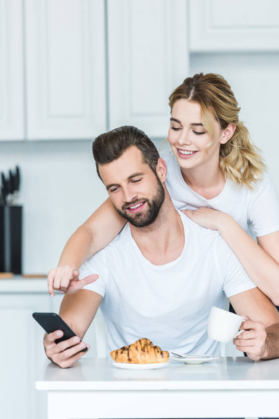 beautiful happy young couple using smartphone while having breakfast together - Zdjęcie, obraz
