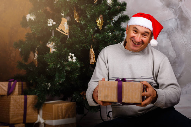 Opa sitzt neben Weihnachtsbaum mit Geschenkschachtel - Foto, Bild