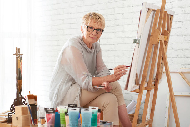 Portrait of smiling aged woman painting in studio - Foto, imagen