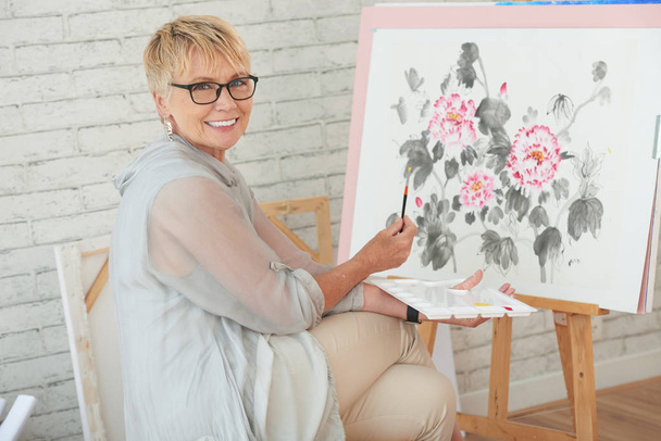 Portrait of happy creative senior woman painting on canvas - Фото, изображение