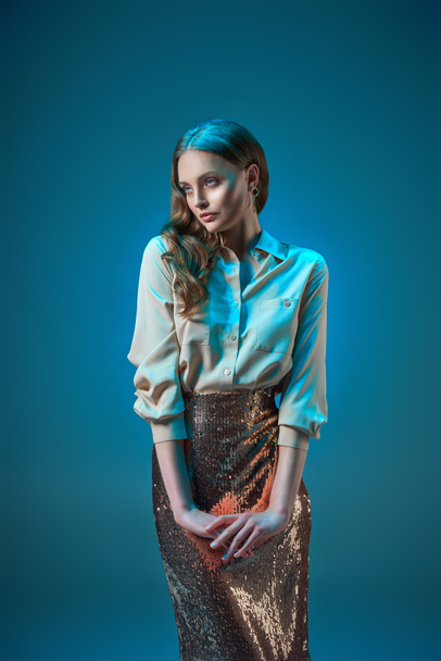 beautiful woman in fashionable golden glittering skirt looking away isolated on blue    - Фото, изображение