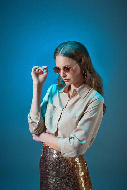 beautiful woman in stylish outfit and sunglasses posing isolated on blue - Foto, afbeelding