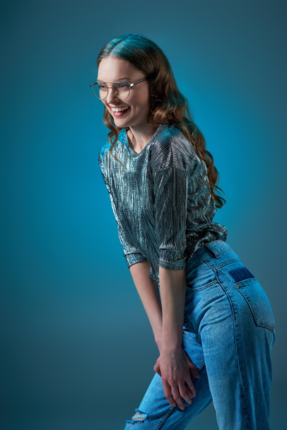 beautiful smiling woman in stylish outfit laughing and looking away isolated on blue - Fotografie, Obrázek