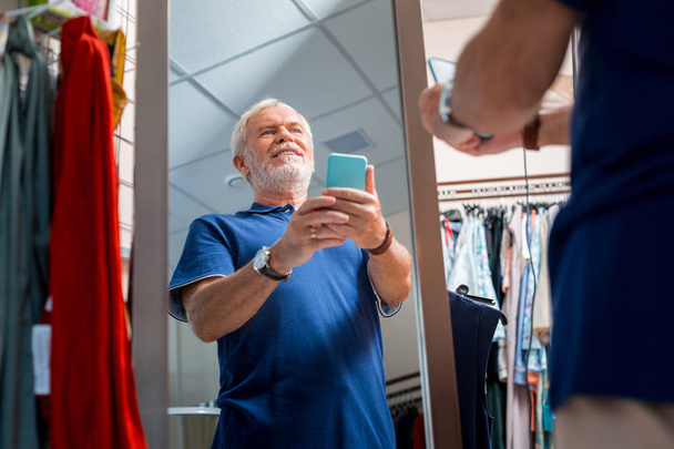 Joyful grey haired man admiring his reflection in shopping store - Фото, изображение