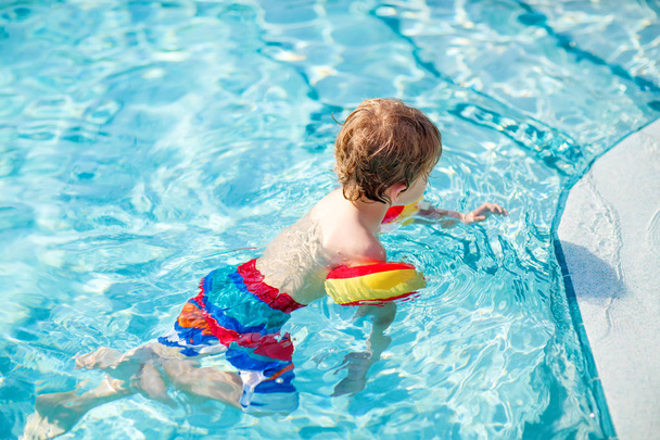 Happy little kid boy having fun in an swimming pool. Active happy child learning to swim. with safe floaties or swimmies. Family, vacations, summer concept - Foto, Imagem