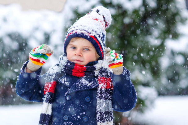 Niedliche kleine lustige Kind in bunten Wintermode Kleidung Spaß haben und spielen mit Schnee, im Freien bei Schneefall. Aktive Freizeitgestaltung im Freien mit Kindern. Junge und Kleinkind fangen Schneeflocken. - Foto, Bild