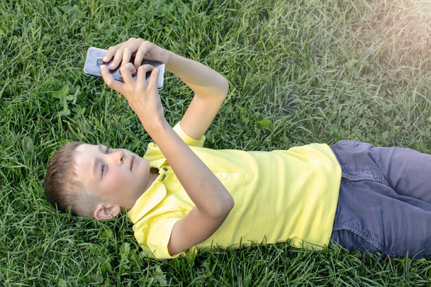 A boy in yellow shirt with cell phone, smartphone lying on the grass. - Fotó, kép