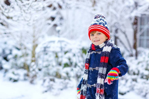 Cute little funny dziecko w kolorowe ubrania mody zimowej zabawy i zabawy ze śniegiem, na zewnątrz podczas opadów śniegu. Aktywny wypoczynek na świeżym powietrzu z dziećmi. Chłopiec i maluch łapie płatki śniegu. - Zdjęcie, obraz