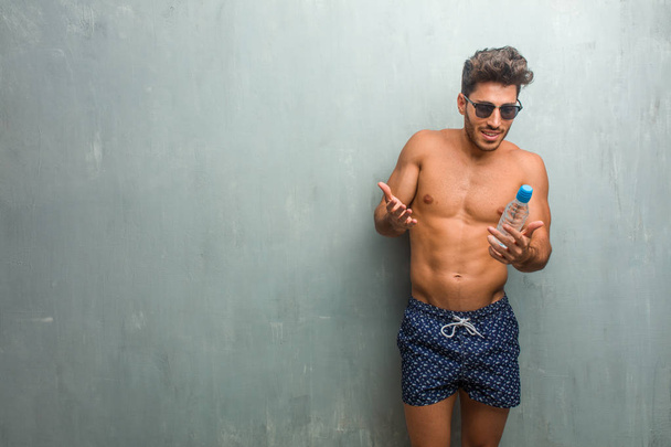 junger athletischer Mann im Badeanzug vor einer Grunge-Wand überrascht und schockiert, mit großen Augen blickend, begeistert von einem Angebot oder einem neuen Job, Gewinnkonzept - Foto, Bild
