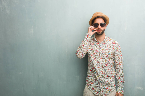 Νεαρός ταξιδιώτης άνθρωπος φορώντας ένα πολύχρωμο πουκάμισο κρατώντας ένα μυστικό ή να ζητήσετε τη σιωπή, σοβαρό πρόσωπο, υπακοή έννοια - Φωτογραφία, εικόνα