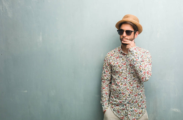 Young traveler man wearing a colorful shirt doubting and confused, thinking of an idea or worried about something - 写真・画像