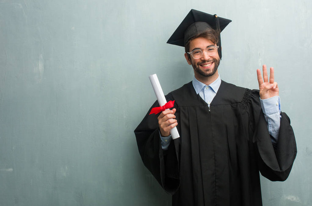 Jeune homme diplômé contre un mur grunge avec un espace de copie montrant numéro trois, symbole de comptage, concept de mathématiques, confiant et joyeux
 - Photo, image