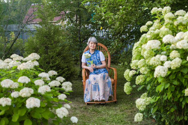 Pretty old woman resting in garden in rocking chair - Foto, Imagem