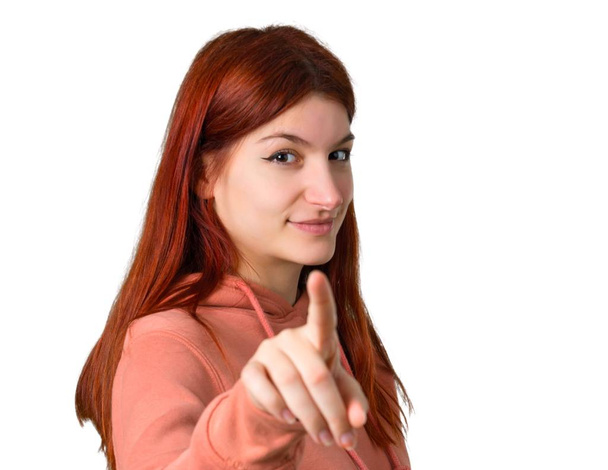 Jeune fille rousse avec sweat-shirt rose pointe doigt vers vous avec une expression confiante sur fond blanc isolé
 - Photo, image