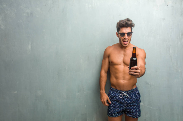 Young athletic man wearing a swimsuit against a grunge wall very angry and upset, very tense, screaming furious, negative and crazy - Zdjęcie, obraz