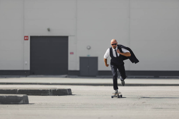 Confident young businessman in business suit on longboard hurrying to his office, on the street in the city - Foto, afbeelding