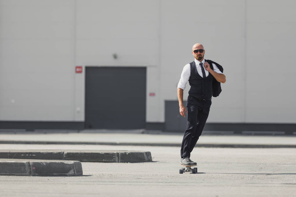 Confident young businessman in business suit on longboard hurrying to his office, on the street in the city - Foto, imagen