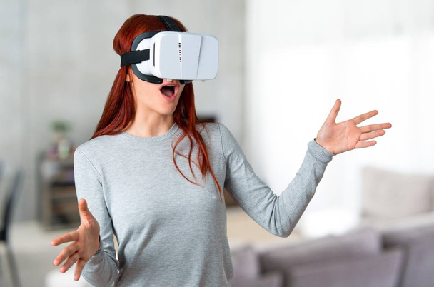 Young redhead girl using VR glasses. Virtual reality experience on unfocused background - Fotografie, Obrázek