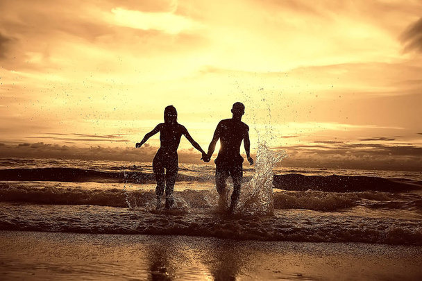 silhouettes of young happy lovers at sandy beach, sunset view . Honeymoon of newlyweds at sea resort.  - Photo, Image