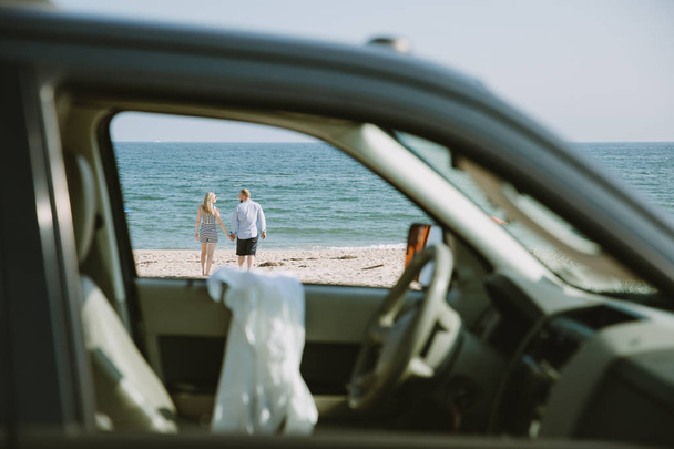 happy couple walking on sea beach, view from car - Foto, afbeelding