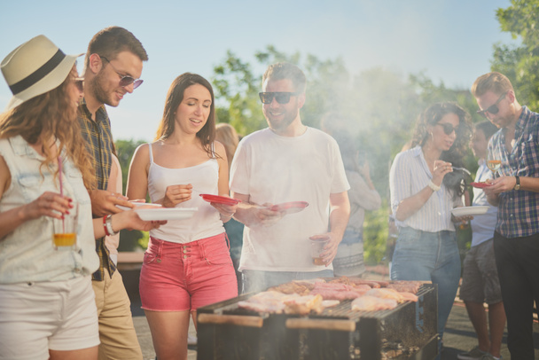 Emberek csoportja áll körül grill, csevegés, ivás és evés.  - Fotó, kép
