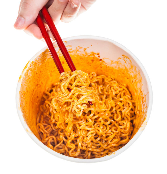 hand keeps red chopsticks with cooked spicy instant noodles isolated on white background - Photo, Image