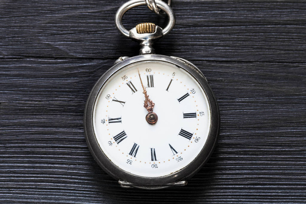 дві хвилини до 12 годин на старовинному кишеньковому годиннику на чорному дерев'яному фоні
 - Фото, зображення