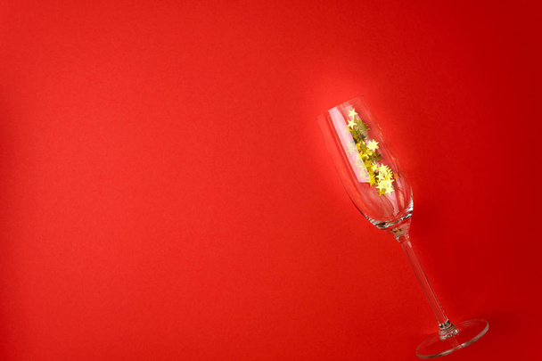 Wineglasses for champagne with golden star shape confetti lying on red paper background. New Year celebration concept. Top view. Flat lay. - 写真・画像