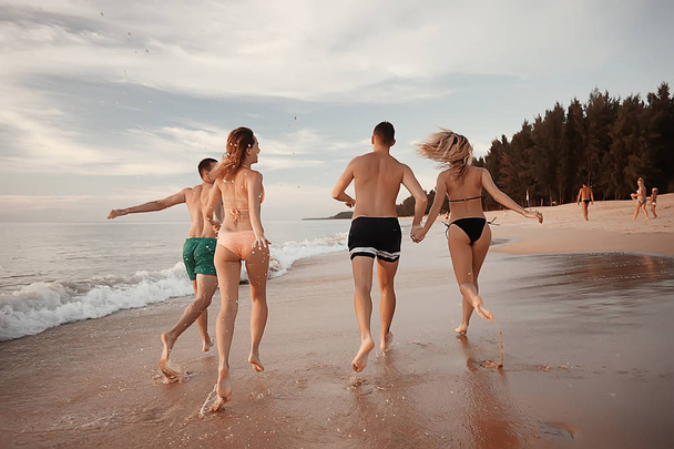 τέσσερις φίλοι που τρέχει στην παραλία, καλοκαιρινές διακοπές και ευτυχία έννοια. Νεαροί άνδρες και γυναίκες τη διασκέδαση στη θάλασσα ακτή - Φωτογραφία, εικόνα