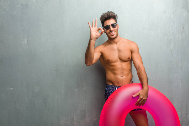 Молодий атлетичний чоловік у купальнику проти гранжевої стіни веселий і впевнений у тому, що робить нормальний жест, схвильований і кричущий, концепція схвалення і успіху
 - Фото, зображення