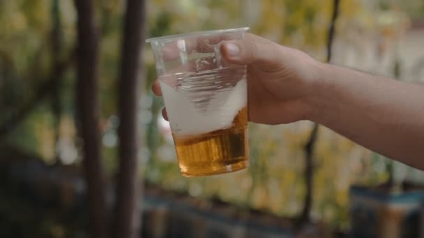 Man Hand houden en langzaam schudden een transparante Plastic beker met Light bier  - Video