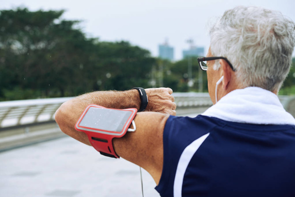 Rear view of elderly runner checking heart rate on fitness tracker when training - 写真・画像