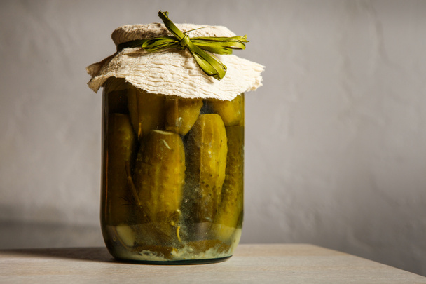 homemade canned cucumbers in small  glass jar stand on kitchen table against gray wall background - Photo, Image