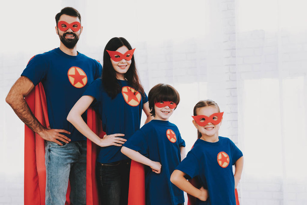 Young Family In Superhero Suits. Posing Concept. Masks And A Raincoats. Bright Room. Resting Together. Save The World. Get Ready. Arms Akimbo. Kids With A Parents. Active Lifestyle. - Photo, Image