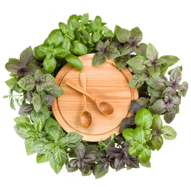 Round wooden cutting board with spoons. Various sweet basil herb leaves edged.. Healthy food concept. Top view. - Photo, Image