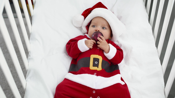adorable baby in santa costume holding christmas toy, mother touching ball - Footage, Video