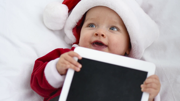чарівна дитина в костюмі Санти грає з планшетом з порожнім екраном в ліжечку вдома, різдвяна концепція
 - Кадри, відео