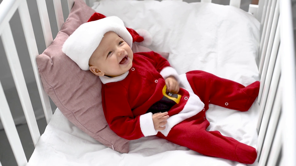 мать трогает лоб улыбающегося очаровательного ребенка в костюме Санта-Клауса в кроватке дома, рождественская концепция
 - Кадры, видео