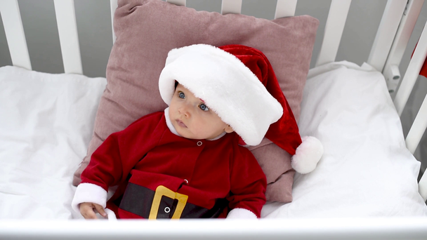 yllättynyt ihana vauva puvussa katselee pois ja istuu pinnasängyssä kotona, joulun konsepti
 - Materiaali, video