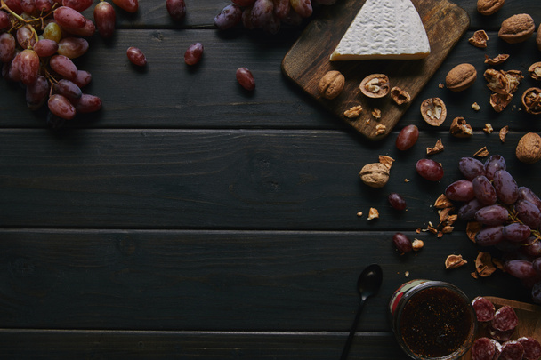 top view of fresh ripe grapes, walnuts, sliced salami, jam and delicious cheese on wooden background   - Photo, Image